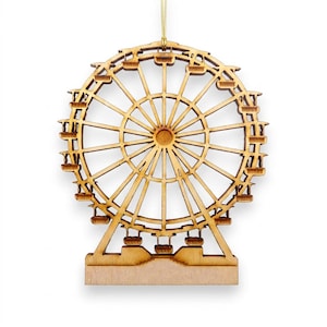 May include: A laser-cut wooden ornament shaped like a Ferris wheel with a circular frame, radiating spokes, and small hanging passenger cars. The natural light brown wood features a smooth finish and is suspended by a thin gold string at the top.