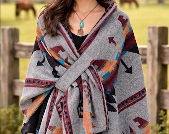 May include: A gray wrap featuring a geometric pattern in shades of orange, maroon, black, and teal. The wrap is worn over a black top and blue jeans, paired with a brown cowboy hat and a turquoise pendant necklace on a thin metal chain.