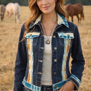 May include: A dark blue denim jacket featuring a light-colored collar, chest pocket flaps, and vertical side panels adorned with a geometric pattern in shades of turquoise, orange, and cream. The jacket has metal buttons and long sleeves with cuffs.