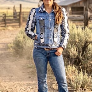 Könnte beinhalten: Eine Jeansjacke mit langen Ärmeln in schwarz-weißem geometrischem Muster, einer Knopfleiste vorne sowie passenden gemusterten Einsätzen an Brust und Saum. Die Jacke wird mit einer blauen Jeans und einem grauen Cowboyhut mit hellblauem Band kombiniert.