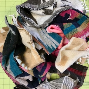 May include: A pile of colorful fabric scraps in various shades of blue, brown, pink, and white. The fabric has a woven pattern and is likely from a blanket or throw.