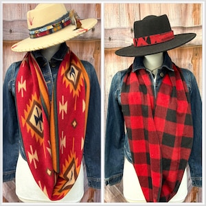 May include: Two hats and scarves are displayed on mannequins. One hat is beige with a patterned band and feathers. The other is black with a red patterned band. The scarves are red, one with a geometric pattern and the other with a black and red plaid pattern.