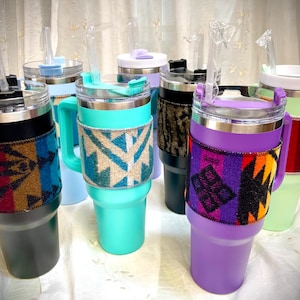 May include: A collection of insulated tumblers in various colors, each with a patterned fabric sleeve. The tumblers have clear lids, handles, and reusable straws. Colors include teal, purple, black, and light blue.