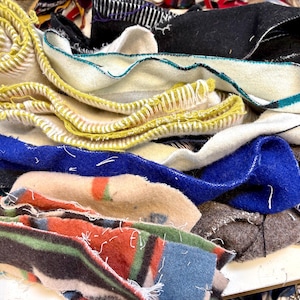 May include: A pile of colorful fabric scraps with different textures and patterns, including blue, yellow, white, and brown. The fabric scraps are arranged in a random order and some have frayed edges.