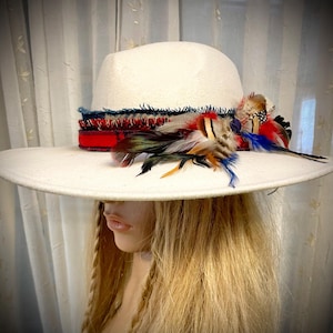 May include: A wide-brimmed white felt hat with a red, blue, and white plaid band and a variety of feathers in shades of brown, white, and blue.