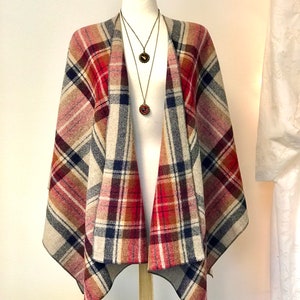 May include: A plaid shawl in shades of red, brown, and beige with a black and white plaid pattern. The shawl is draped over a mannequin and has a fringed edge.