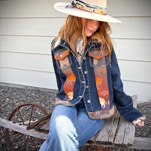 Op de afbeelding: Een vrouw draagt een blauw denim jack met een kleurrijke, gepatenteerde voering, blauwe jeans en een witte cowboyhoed met een verenaccent.