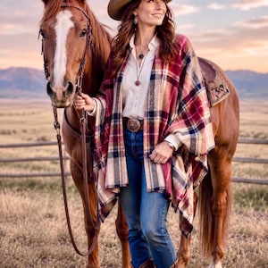 May include: A person wearing a tan cowboy hat, a cream-colored button-down shirt, blue jeans, and a red, navy, and cream plaid poncho. The person is standing next to a brown horse with a white blaze on its face, wearing a leather bridle and saddle.