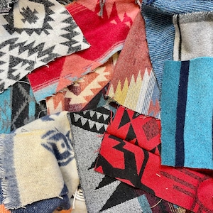 May include: A collection of colorful fabric scraps with geometric patterns, including red, blue, black, and white. The fabrics are arranged in a random pattern, creating a visually interesting and textured background.