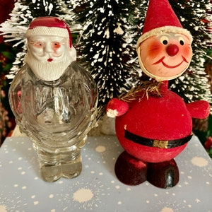 May include: Two vintage Christmas decorations, a glass Santa Claus bottle and a red felt Santa Claus figure. The glass Santa Claus bottle is clear and has a red hat and white beard. The red felt Santa Claus figure has a red hat, a white beard, and a black belt. Both figures are smiling.