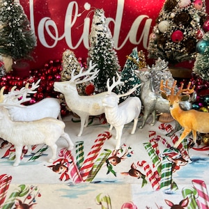 May include: Five vintage plastic reindeer figurines, four white and one brown, with antlers, standing on a white and red candy cane patterned surface.