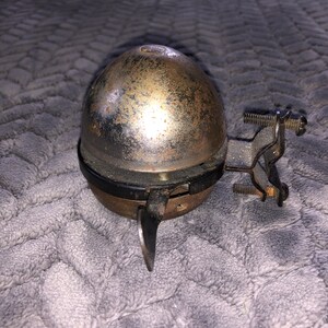 May include: A vintage bicycle bell with a silver dome and a black metal bracket. The bell has a rusty patina and a small lever on the side.