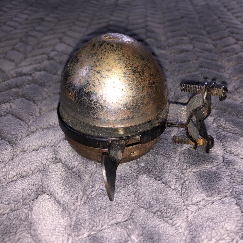 May include: A vintage bicycle bell with a silver dome and a black metal bracket. The bell has a rusty patina and a small lever on the side.