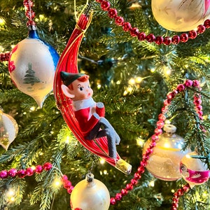 May include: A Christmas tree decorated with red and white ornaments, including a vintage elf ornament hanging from a red and white string. The tree is also decorated with a string of red beads.