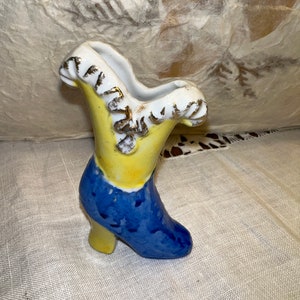 May include: A ceramic boot-shaped vase with a yellow, blue, and white glaze. The vase has a ruffled top and a high heel.