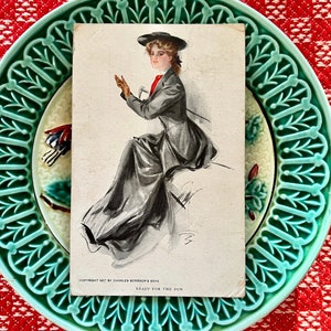 Dama elegante en relieve con traje de montar largo y negro sentada en el banco del carruaje "Listo para la carrera" 1907 Postal c. Charles Scribner & Sons.