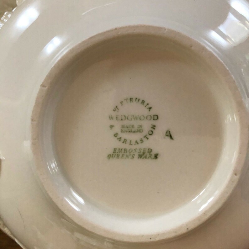 Pu&ograve; includere: Un piatto in ceramica bianca con un marchio stampato in verde che recita "Wedgwood, Made in England, Barlaston, Embossed Queen's Ware".