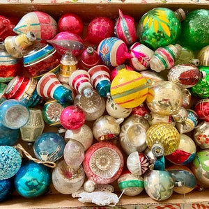 Pode incluir: Uma caixa cheia de enfeites de Natal vintage em várias cores e designs, incluindo vermelho, verde, azul, prata e dourado. Os enfeites são feitos de vidro e têm uma variedade de formas, incluindo redonda, sino e estrela.