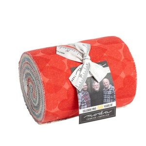 May include: A roll of red fabric with a white and grey pattern. The fabric is tied with a white ribbon and has a label that says "Celebrating 50 Years of Moda Fabrics & Supplies".