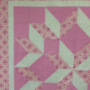 Puede incluir: Una colcha rosa y blanca con un patr&oacute;n geom&eacute;trico. La colcha est&aacute; hecha de cuadrados y tri&aacute;ngulos, y el patr&oacute;n se repite en toda la colcha.