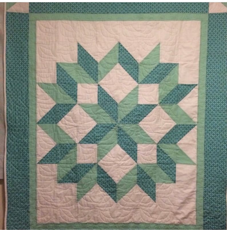 Puede incluir: Una colcha con un patr&oacute;n de estrella en forma de estallido en tonos de verde y blanco. La colcha est&aacute; hecha con una variedad de telas y tiene un dise&ntilde;o acolchado.