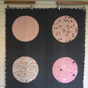 May include: A grey and pink quilt with four large circles. Each circle features a different pink and white patterned fabric. The quilt has a black and white trim.