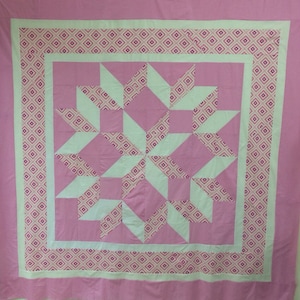 Puede incluir: Una colcha rosa y blanca con un patr&oacute;n geom&eacute;trico. La colcha est&aacute; hecha de cuadrados y tri&aacute;ngulos, y el patr&oacute;n se repite en toda la colcha.