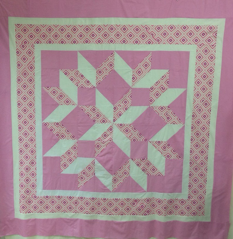 Puede incluir: Una colcha rosa y blanca con un patr&oacute;n geom&eacute;trico. La colcha est&aacute; hecha de cuadrados y tri&aacute;ngulos, y el patr&oacute;n se repite en toda la colcha.