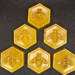 May include: Six hexagonal honey-coloured wax melts, each featuring a raised bee design. The wax melts are arranged in a triangular pattern.