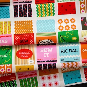 May include: A white fabric featuring a repeating grid pattern of vintage-style sewing notions packaging. Each rectangular block displays colourful graphics, including text like STITCH THIS, RIC RAC, SEW IT, and SINGLE FOLD, alongside floral, polka dot, and wavy line prints.