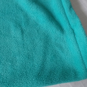 May include: Close-up of a teal blue fleece fabric with a stitched edge.