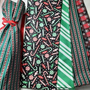 May include: Set of five fabric gift bags with a Christmas theme. The bags feature a variety of patterns, including candy canes, peppermint swirls, and stripes in red, green, and white.