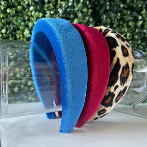 Puede incluir: Tres diademas de terciopelo en azul, rojo y estampado de leopardo. Las diademas están apiladas una encima de la otra.