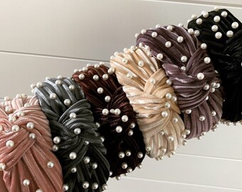 May include: A set of seven velvet headbands with pearl embellishments. The headbands are in various colors, including pink, gray, brown, beige, and purple.