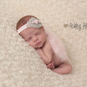 May include: A sleeping baby girl wearing a pink feather boa and a sparkly headband with pink flowers. The baby is lying on a white, fluffy blanket.