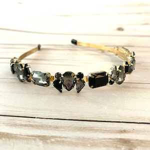 May include: A gold headband with black and gray rhinestones. The headband is decorated with a variety of shapes and sizes of rhinestones.