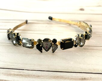 May include: A gold headband with black and gray rhinestones. The headband is decorated with a variety of shapes and sizes of rhinestones.