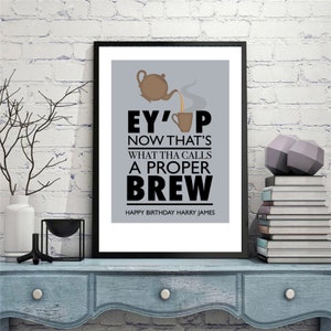 May include: A framed print with a gray background and black text that reads "Ey' up now that's what tha calls a proper brew". The text is accompanied by a cartoon image of a teapot pouring tea into a cup. The bottom of the print reads "Happy Birthday Harry James".