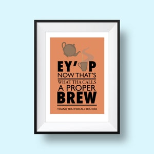 May include: A framed print with an orange background and a black teapot pouring tea into a cup. The text reads "Ey'up Now That's What Tha Calls A Proper Brew" and "Thank You For All You Do".