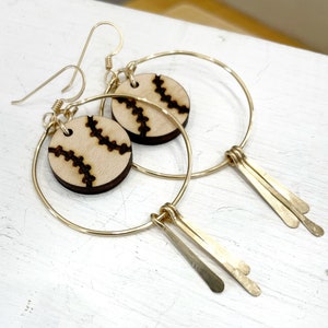 May include: Gold hoop earrings with a wooden baseball charm and gold fringe.