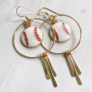 May include: Gold-tone hoop earrings featuring white baseball charms with red stitching. Each earring has three gold-tone dangling bars. The earrings are designed with a hook closure.