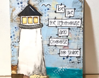 May include: A mixed media painting of a white lighthouse with a black roof and yellow windows. The lighthouse is on a rocky shore with blue water. The text "Be like the lighthouse and choose to shine" is written in black marker on a white background.
