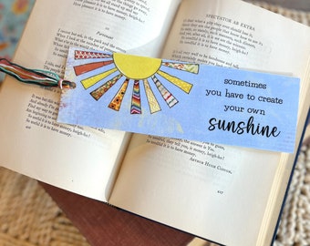 May include: A blue and yellow bookmark with a sun design and the text "sometimes you have to create your own sunshine".