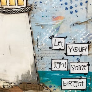May include: A mixed media art piece featuring a white lighthouse with yellow windows and a black roof. The background includes blue paint, text, and collage elements. Five white rectangular paper cutouts display the text: Let YOUR light shine bRight.