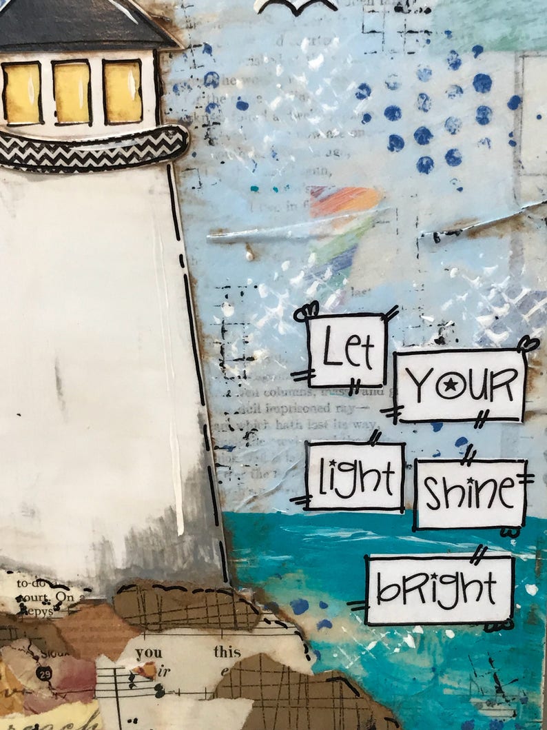 May include: A mixed media art piece featuring a white lighthouse with yellow windows and a black roof. The background includes blue paint, text, and collage elements. Five white rectangular paper cutouts display the text: Let YOUR light shine bRight.
