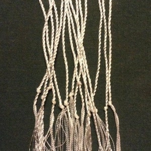 May include: A bundle of white tassel cords with a twisted rope design. The cords are tied together at the top and have long, thin tassels.