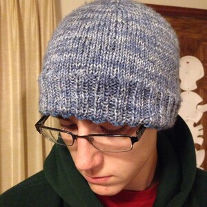 May include: A person wearing a blue and white knitted hat with a dark green hooded sweatshirt.