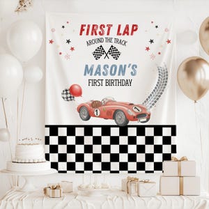 May include: A white fabric backdrop featuring a red race car with the number 1, black and white checkered flags, and the text FIRST LAP AROUND THE TRACK MASON'S FIRST BIRTHDAY. The bottom section has a black and white checkered pattern design.