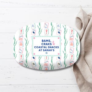 May include: An oval serving platter with a white background, featuring a repeating pattern of playing cards, seahorses, and seaweed. The center has text that reads "BAMS, CRAKS & COASTAL SNACKS AT SARAH'S".