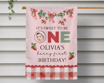 May include: A pink garden flag featuring a watercolor strawberry vine with red bows, a circular photo of a baby, and the text IT'S SWEET TO BE ONE OLIVIA'S berry first BIRTHDAY. The bottom border has a red and white gingham check pattern.